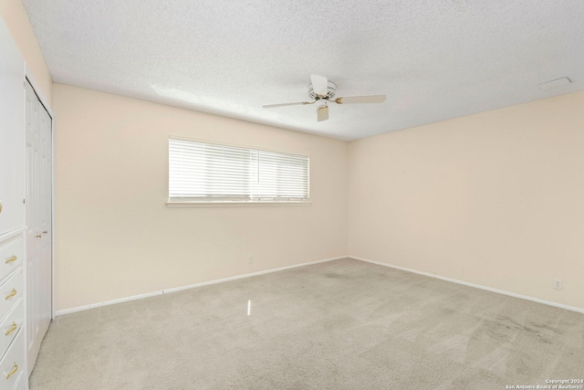 unfurnished bedroom with baseboards, light colored carpet, ceiling fan, a textured ceiling, and a closet