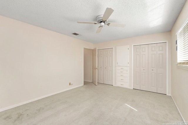 unfurnished bedroom featuring light carpet, baseboards, visible vents, a textured ceiling, and multiple closets