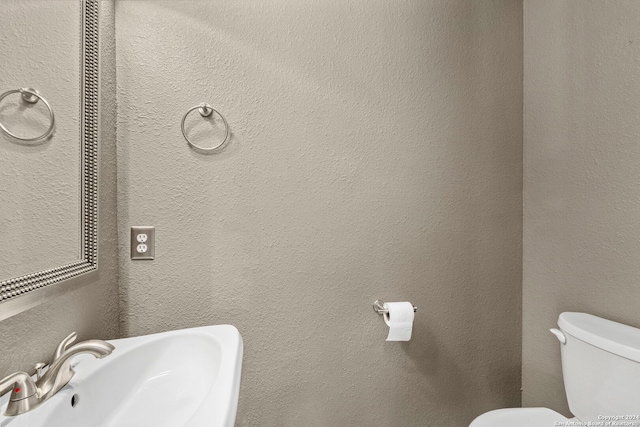 bathroom with a textured wall, a sink, and toilet