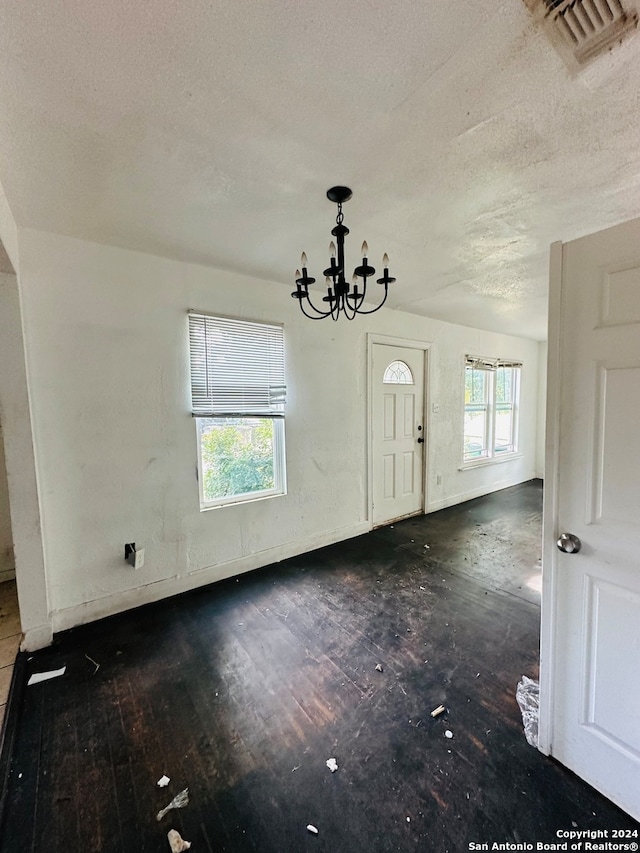 spare room featuring plenty of natural light, a textured ceiling, a chandelier, and wood-type flooring