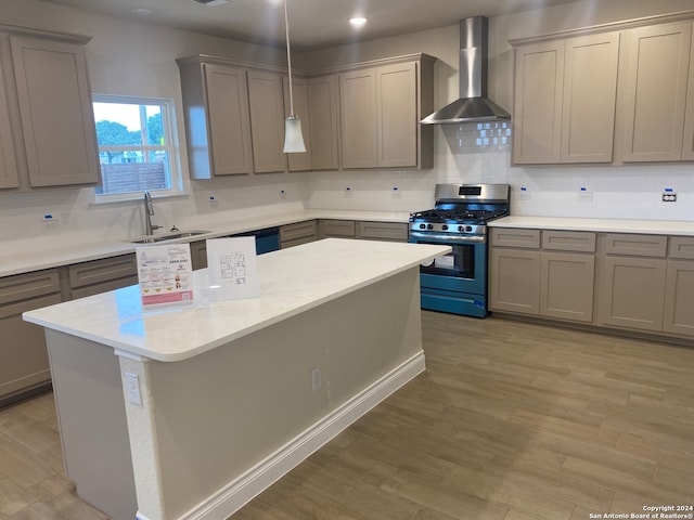 kitchen featuring light hardwood / wood-style floors, decorative backsplash, wall chimney exhaust hood, sink, and stainless steel gas range oven