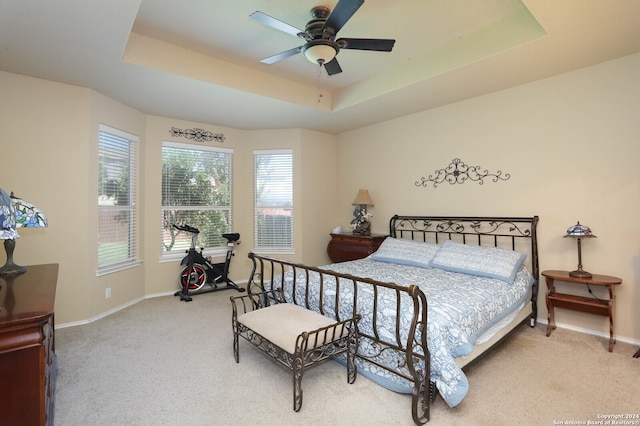 bedroom with a tray ceiling, light colored carpet, and ceiling fan