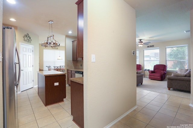 kitchen with ceiling fan with notable chandelier, hanging light fixtures, light tile patterned floors, a kitchen island, and stainless steel refrigerator