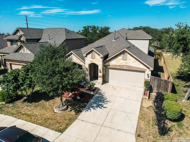 view of front facade featuring a garage, a shingled roof, concrete driveway, stone siding, and fence