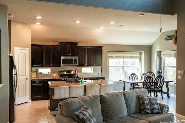 kitchen featuring fridge, a kitchen island with sink, light tile patterned floors, sink, and stove