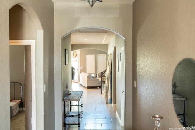 corridor with arched walkways, a textured wall, and light tile patterned floors