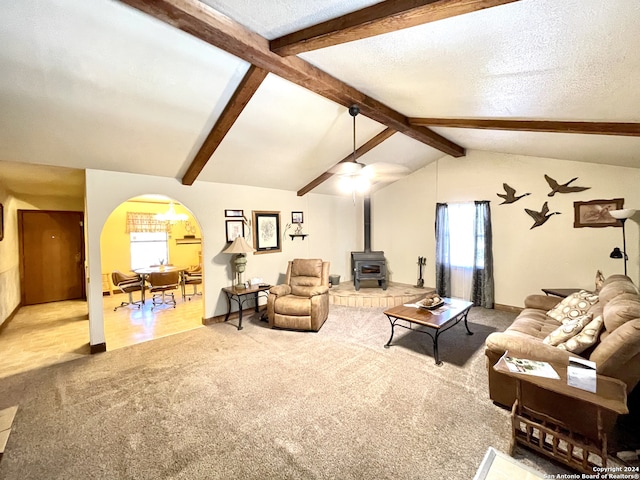 living room featuring a wood stove, a healthy amount of sunlight, vaulted ceiling with beams, and a textured ceiling