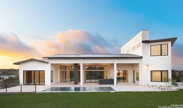 back house at dusk featuring a lawn and a patio area