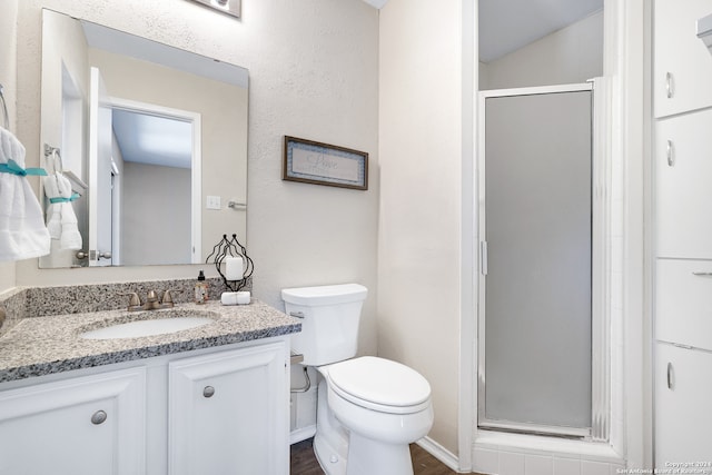 bathroom featuring wood-type flooring, a shower with door, vanity, and toilet