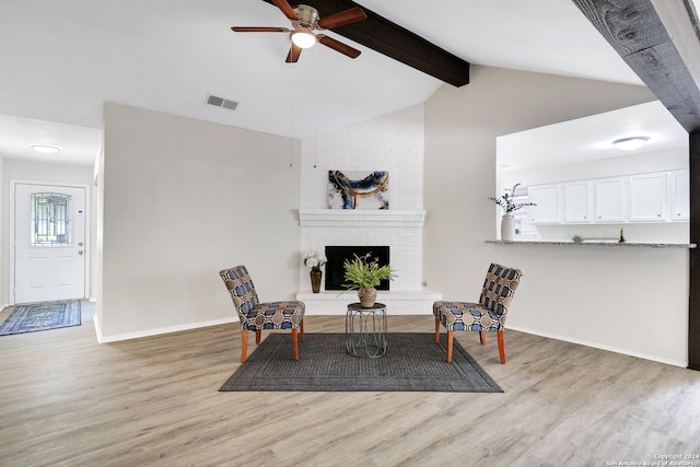 sitting room with brick wall, light wood-type flooring, a fireplace, vaulted ceiling with beams, and ceiling fan