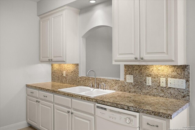 kitchen featuring decorative backsplash, white cabinets, light stone counters, white dishwasher, and sink