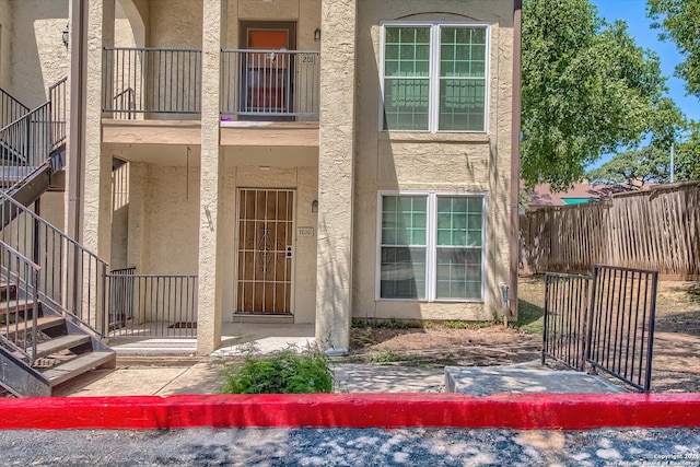 property entrance featuring fence, a balcony, and stucco siding