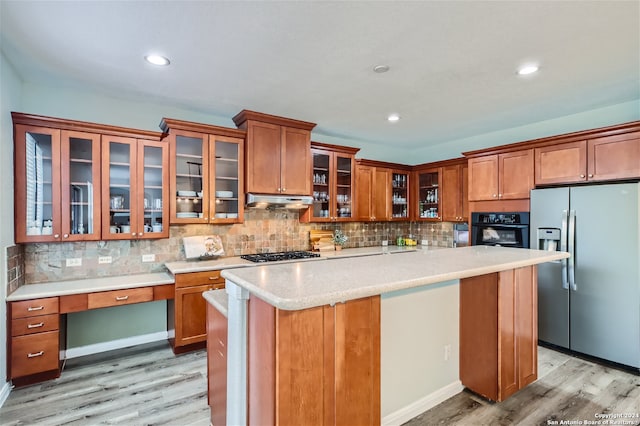 kitchen featuring brown cabinetry, stainless steel appliances, light countertops, light wood-type flooring, and under cabinet range hood