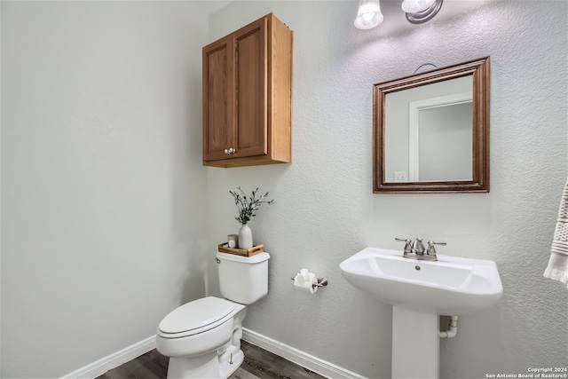 half bathroom with a sink, toilet, baseboards, and wood finished floors