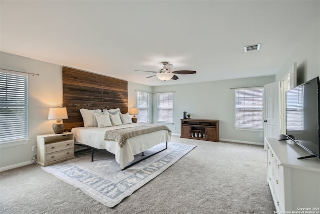 carpeted bedroom featuring multiple windows, ceiling fan, and wooden walls