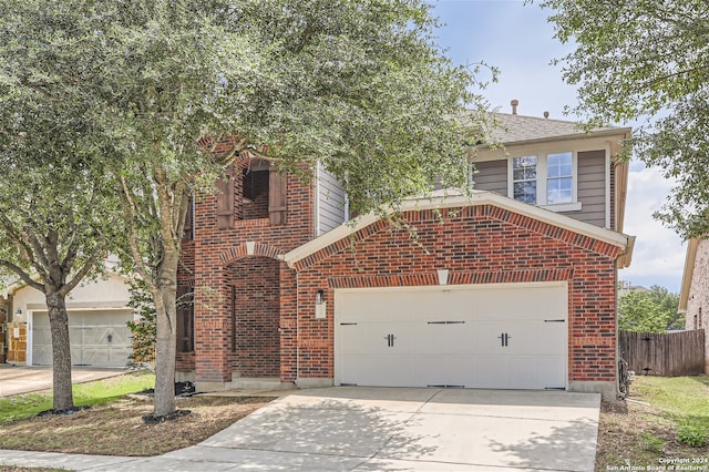 traditional-style home with brick siding, driveway, an attached garage, and fence