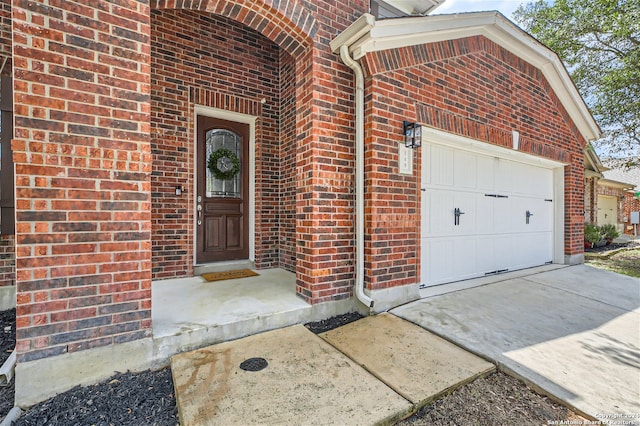 doorway to property with a garage, driveway, and brick siding