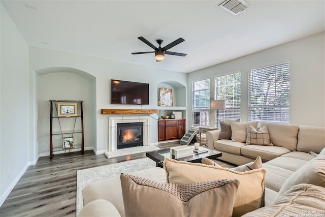 living area featuring wood finished floors, visible vents, baseboards, a ceiling fan, and a glass covered fireplace