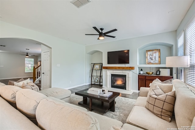 living area with arched walkways, wood finished floors, visible vents, a ceiling fan, and a glass covered fireplace