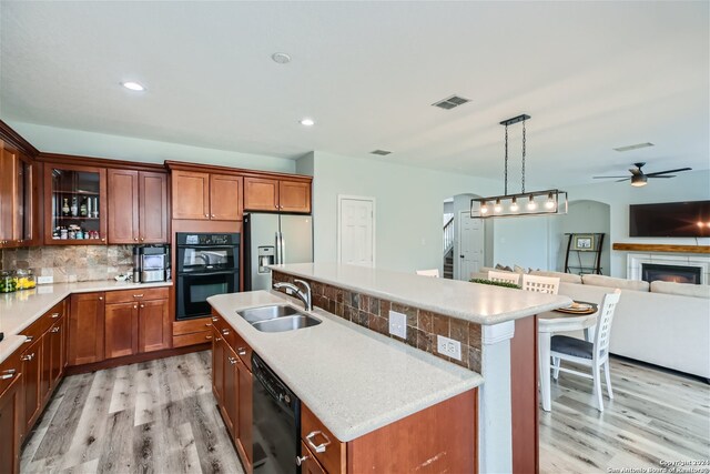 kitchen featuring light hardwood / wood-style floors, sink, black appliances, decorative backsplash, and a kitchen island with sink