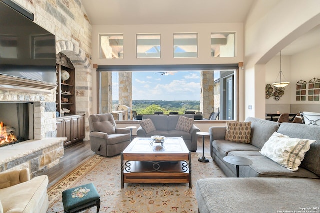 living room featuring hardwood / wood-style floors, high vaulted ceiling, a stone fireplace, and built in features