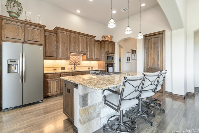 kitchen with high vaulted ceiling, appliances with stainless steel finishes, light hardwood / wood-style floors, tasteful backsplash, and hanging light fixtures