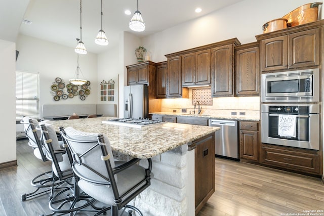 kitchen with light wood-type flooring, backsplash, a kitchen bar, light stone counters, and stainless steel appliances