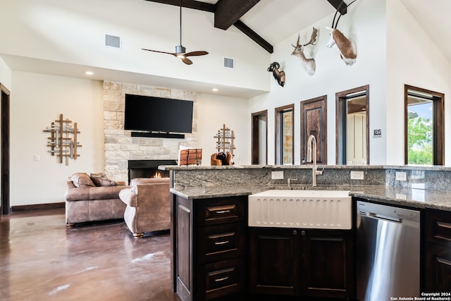 kitchen featuring stainless steel dishwasher, sink, beamed ceiling, ceiling fan, and a stone fireplace