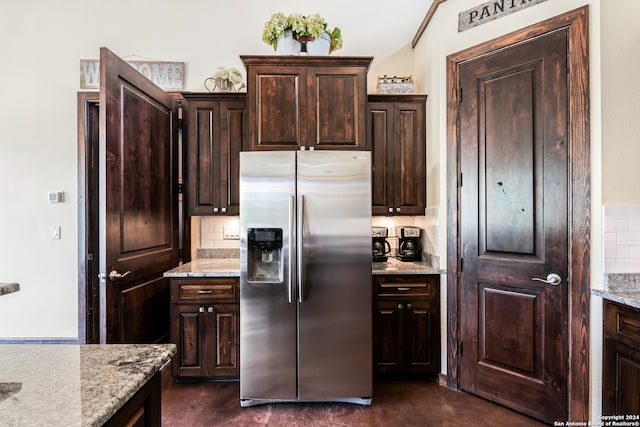 kitchen featuring decorative backsplash, light stone counters, stainless steel fridge, and dark brown cabinetry