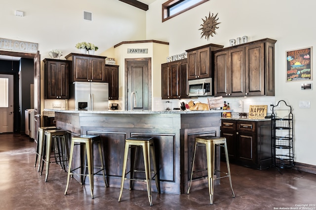 kitchen featuring a breakfast bar area, stainless steel appliances, light stone countertops, and dark brown cabinetry