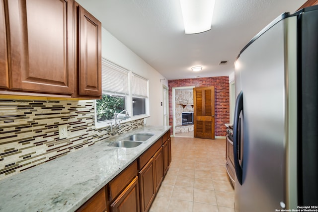 kitchen featuring a large fireplace, stainless steel refrigerator, sink, brick wall, and light tile patterned floors