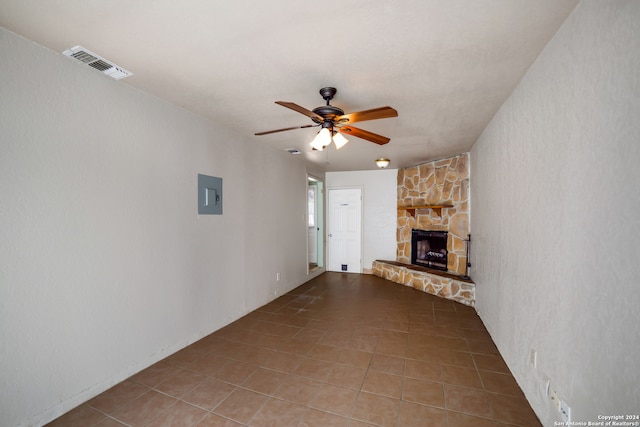 unfurnished living room with ceiling fan, a stone fireplace, electric panel, and tile patterned floors