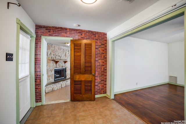 unfurnished living room featuring brick wall, a textured ceiling, tile patterned floors, and a fireplace