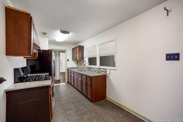 kitchen with sink, decorative backsplash, light tile patterned floors, and gas range oven