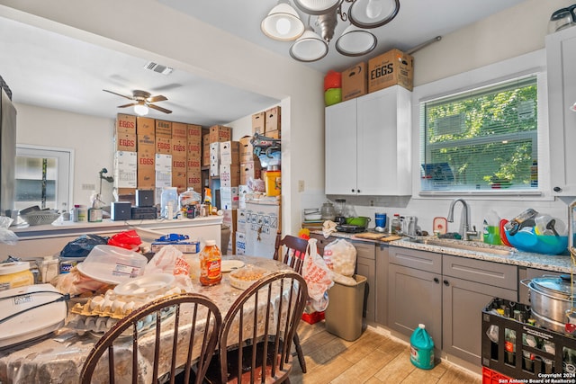 kitchen with sink, light hardwood / wood-style flooring, light stone counters, ceiling fan with notable chandelier, and gray cabinetry