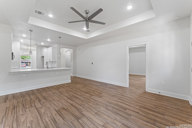 unfurnished living room featuring light wood-type flooring, ceiling fan with notable chandelier, and a tray ceiling