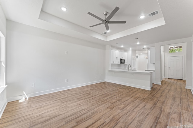 unfurnished living room with ceiling fan, a raised ceiling, sink, and light hardwood / wood-style floors