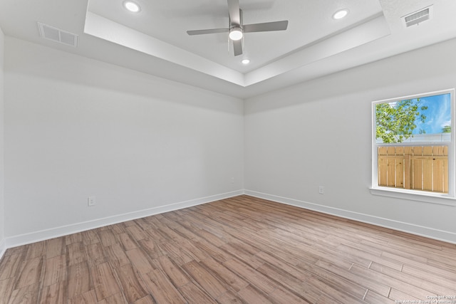 unfurnished room with ceiling fan, light hardwood / wood-style flooring, and a tray ceiling