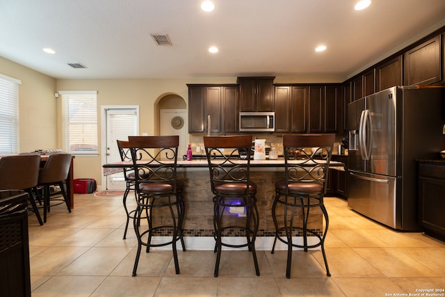 kitchen featuring appliances with stainless steel finishes, dark brown cabinetry, a breakfast bar area, and an island with sink