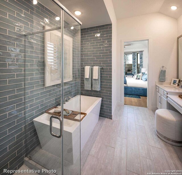 bathroom featuring independent shower and bath, vanity, tile walls, hardwood / wood-style flooring, and lofted ceiling