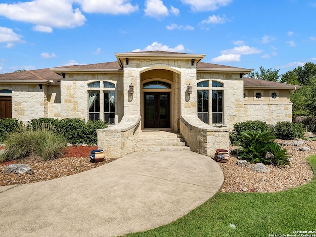 prairie-style house featuring stone siding, french doors, and a shingled roof