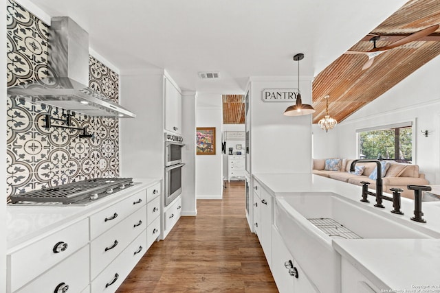 kitchen featuring appliances with stainless steel finishes, light countertops, wall chimney exhaust hood, and white cabinetry