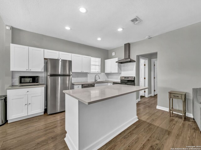 kitchen featuring appliances with stainless steel finishes, hardwood / wood-style flooring, white cabinets, and wall chimney exhaust hood