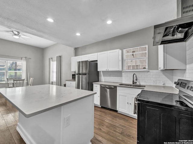 kitchen featuring white cabinetry, a center island, sink, appliances with stainless steel finishes, and wall chimney range hood