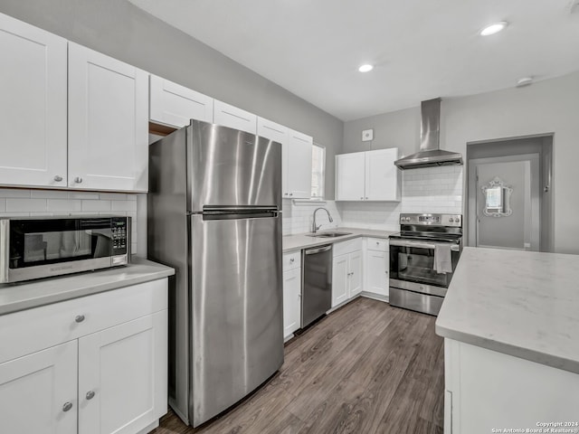 kitchen featuring appliances with stainless steel finishes, wood-type flooring, wall chimney exhaust hood, white cabinets, and sink