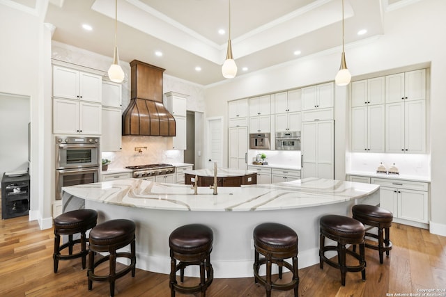 kitchen featuring a spacious island, decorative light fixtures, custom exhaust hood, a tray ceiling, and double oven