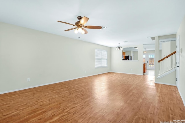 unfurnished living room featuring light wood finished floors, baseboards, a wealth of natural light, and ceiling fan with notable chandelier