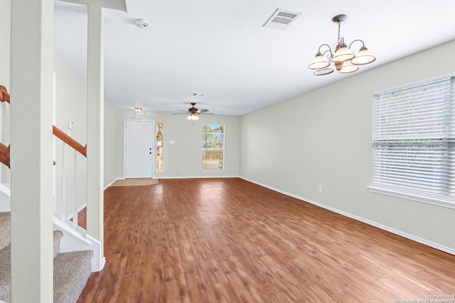 unfurnished living room featuring stairs, visible vents, wood finished floors, baseboards, and ceiling fan with notable chandelier