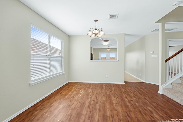 spare room featuring baseboards, visible vents, stairway, wood finished floors, and a notable chandelier