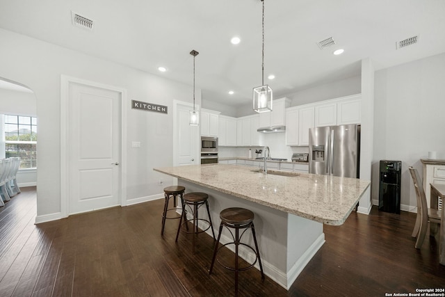 kitchen featuring stainless steel appliances, dark hardwood / wood-style floors, sink, light stone counters, and an island with sink